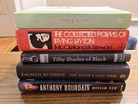 Five hardcover books stacked showing titles and authors: Joe Schwarcz 'An Apple A Day', Irving Layton 'The Collected Poems', Arthur Black 'Fifty Shades of Black', Salman Rushdie 'The Moor's Last Sigh', Anthony Bourdain 'Medium Raw'