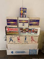 Photo showing stack of seven vintage baseball card boxes, including two 1990 One-Cent Baseball boxes, a Donruss 1991 Collector's Set Baseball Puzzle & Cards box, and additional MLB branded baseball puzzle boxes stacked with a Commander electrical equipment box at the bottom