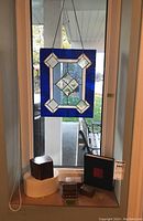 Overall view of stained glass suncatcher hanging in window with four assorted boxes below on ledge.