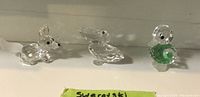 Three Swarovski crystal animals: fox, pelican, and bird figurines, displayed on a white shelf.