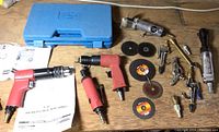 View of the entire set showing 3 pneumatic air tools (red and silver), 6 grinding/cutting discs, 3 drill bits, accessories, and blue plastic case.