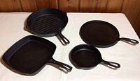 Four cast iron pans displayed on a table including square grill pan, round griddle, small and large skillets.