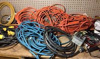Photo showing multiple heavy-duty extension cords in orange, blue, and black coiled on a table with a metal outlet box and some electrical components nearby.