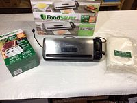 FoodSaver FM3900 vacuum sealer with unopened box of vacuum sealer bags and extra bags displayed with original packaging in background.