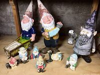 Photo showing all nine gnome figurines including the large purple hat gnome, wheelbarrow gnome, accordion player, and the smaller seated gnomes, some broken.