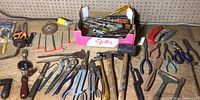 Wide view of various hand tools including hammers, pliers, screwdrivers, box cutters spread on a workbench