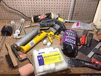 Paint rollers, brushes, caulking guns and sealant tubes, scrapers on wooden table against pegboard background