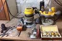 DeWalt router motor with handles, extra stand, plastic attachments, wrenches, and boxed router bits arranged on a workbench.