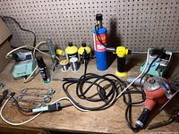 Overview of all items on wooden table including soldering irons, torches, solder wire, and accessories