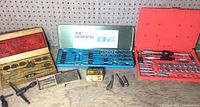 Photo shows three tap and die sets in their respective cases along with additional tools on a wooden surface.