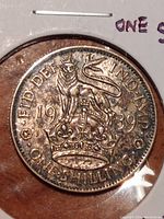 Obverse side of 1939 UK One Shilling coin showing lion standing on a crown, date, and inscriptions.