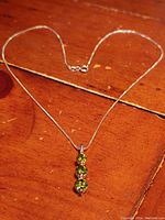 Full view of the 18-inch sterling silver boxlink chain with the peridot trio pendant lying flat on a wooden surface.