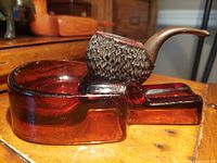 Amber glass pipe holder and ashtray with a hand carved pipe placed in the holder, showing side view of pipe bowl texture and glass color.