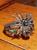 Detailed side-angle photo showing the black widow spider design with prominent black and grey Austrian crystals on a dark silvertone hinged bracelet placed on a wooden surface.