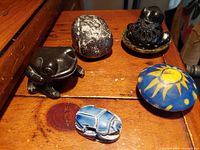 Group of six collectible figurines on wooden surface including stone candle, frogs, beetle, and rock figurines shown from above at angled perspective.