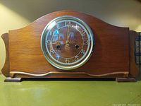 Front view of wooden Enfield mantel clock showing round dial with Arabic numerals, glass cover, winding holes, and clock hands at 9:11.