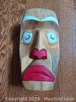 Front view of hand carved and painted Indigenous mask with red, white and black detailing on natural wood base.