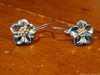 Close-up front view of both floral sterling silver earrings on wooden background showing design detail.