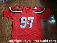Front view of the red NFL jersey with number 97 and shoulder stripes, laid flat on wood floor.