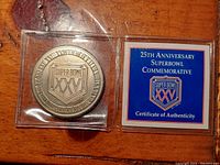 Photo of front side of silver coin featuring Super Bowl XXV logo next to Certificate of Authenticity in a plastic case.