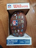 Front and side view of the 11-inch junior football showing the NFL shield logo and multiple individual NFL team logos on brown composite leather.