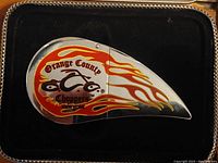 Close-up of silver metallic lighter shaped like a motorcycle gas tank with flame graphics and Orange County Choppers logo on black background inside box