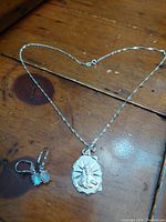 Photo showing the two leverback earrings with oval rainbow moonstones alongside the Sacred Heart pendant on an 18-inch twisted sterling silver chain, on a wooden surface.