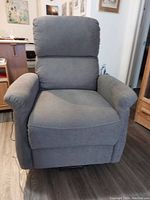 Front view of gray upholstered power lift recliner chair with padded armrests and backrest.