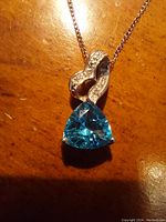 Closeup front view of the electric blue topaz pendant with diamond accents on platinum over sterling silver chain against wood background.