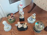 Photo showing all seven vintage music boxes featuring various clown and child figurines arranged on wooden floor.