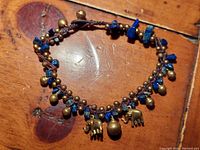 Photo showing woven leather bracelet with brass beads, elephant charms, and lapis lazuli chips on wooden surface.