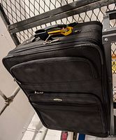 Photo of black 27-inch Atlantic suitcase showing front with two zippered exterior compartments, visible zippers, soft fabric and part of retractable handle and wheels.