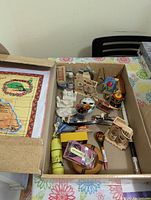 Photo of the first box of souvenirs showing small souvenirs including wooden crafts, decorative spoons, miniature bottles, ceramic hand, and a yellow thermos.