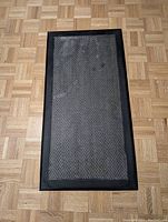 Dark gray anti-fatigue mat with herringbone pattern laid flat on parquet floor