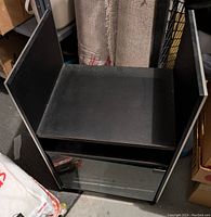 Black cart on wheels with two shelves including a glass door on bottom shelf