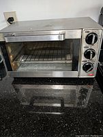 Front view of Hamilton Beach stainless steel toaster oven showing glass door, handle, and three control knobs on right side.