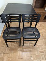 Two black wooden slatted chairs placed side by side on parquet floor.