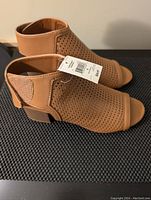 Side view of tan perforated open-toe sandal with zipper closure and tag showing price and size