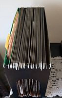 Side view of numerous brown legal size hanging folders with white plastic hooks in a black filing rack.