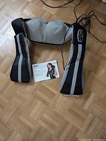 Full view of the TruMedic back massager showing the black and gray fabric, reflective stripes, control panel, and user manual on floor.