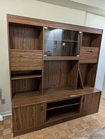 Full front view of the wall unit showing open shelving, glass doors, drawers, and sliding bottom doors.