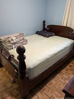 Queen size wood bed frame with mattress and folded bedding on top in bedroom environment