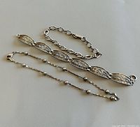 Two silver bracelets and one silver anklet laid out showing links and design.
