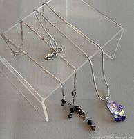 Photo of two sterling silver necklaces displayed on clear acrylic stand; one with black bead filigree pendant, one with purple glass pendant.