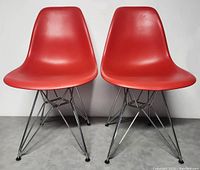 Front view of two red modernist chairs with chrome wire frames placed side by side against a neutral background.