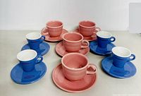 Front and side view of all 8 cups and saucers showing the two pink sets and two blue sets arranged on a table