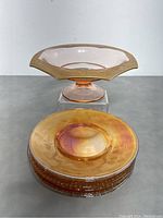 Stack of six iridescent amber carnival plates with footed candy bowl placed above, showing golden hues and reflective surface.