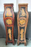 Front view of two antique French wooden pedestals showing marquetry floral inlays and brass side decorations.