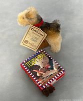 Side view of the terrier plush with certificate and vintage Teddy Bear book showing the front cover of the book and plush.