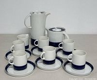 Coffee set arranged with coffee pot, sugar bowl, creamer, 6 cups and 6 saucers displayed on a white surface